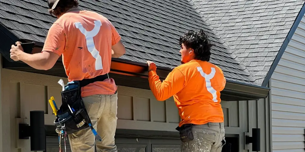 Two Chappell techs on ladders working along a fascia line, seen from behind